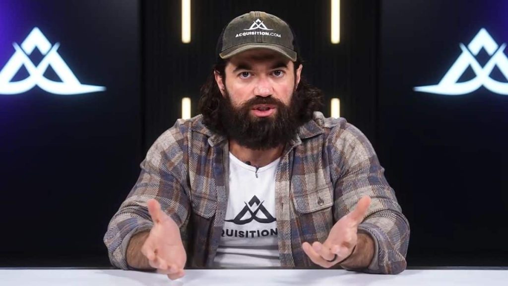 Alex Hormozi en studio portant une casquette et un t-shirt Acquisition.com